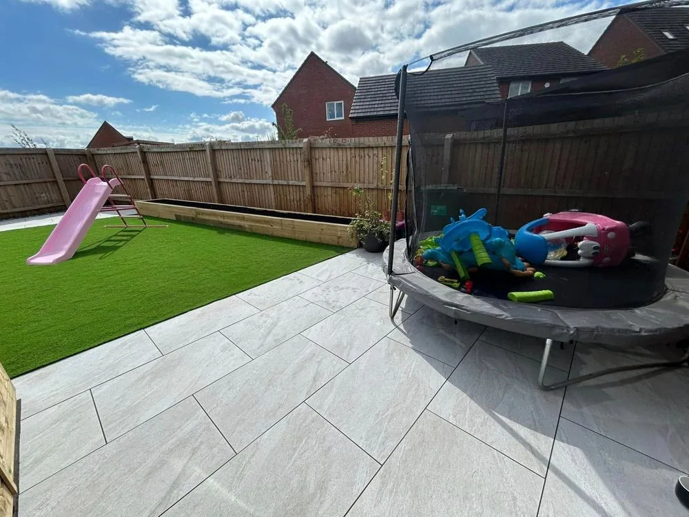 Family garden with artificial lawn, pale paving, a slide, trampoline and raised timber planter