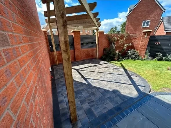 Grey block paving around the base of a timber structure beside a brick house