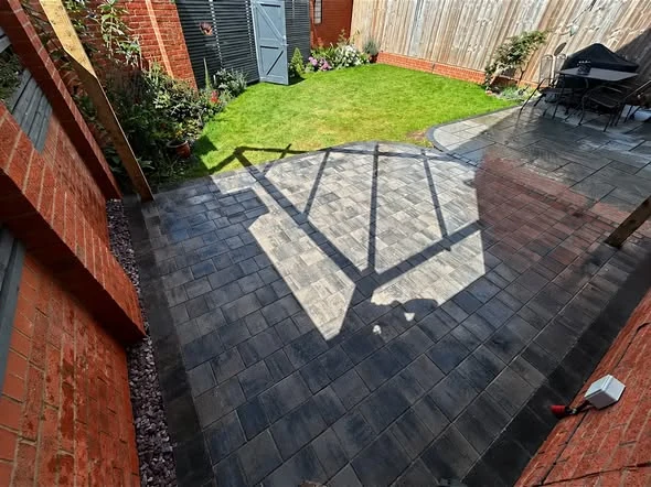 Three-size grey block paved patio beside a lawn and timber garden structure