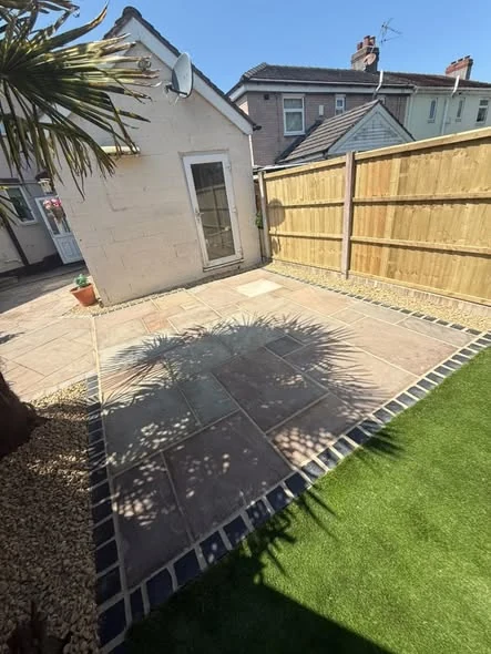 Completed Indian stone patio with a dark edge, artificial lawn and timber boundary in Northwich