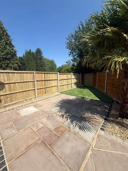 Indian stone patio, dark edging and decorative gravel beside an artificial lawn in Northwich