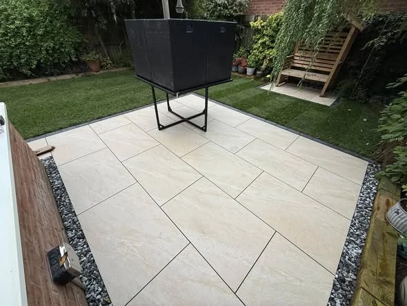 Crema porcelain patio with dark gravel borders beside a freshly turfed lawn